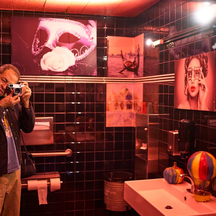 Masquerade in the men's room. Every masked face on the wall is watching, and the guy by the sink brought a camera. Takin